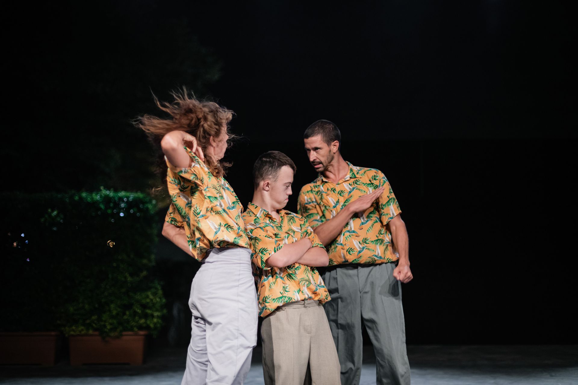 Drei Performer*innen stellen eine Vater-Mutter-Kind Beziehung dar. Die Haare der Mutter (links) fliegen wegen einer Bewegung. Das Kind (Mitte) verschränkt die Arme und sieht vorwurfsvoll zum Vater. Der Vater (rechts) hat den Arm gehoben, scheint wütend.