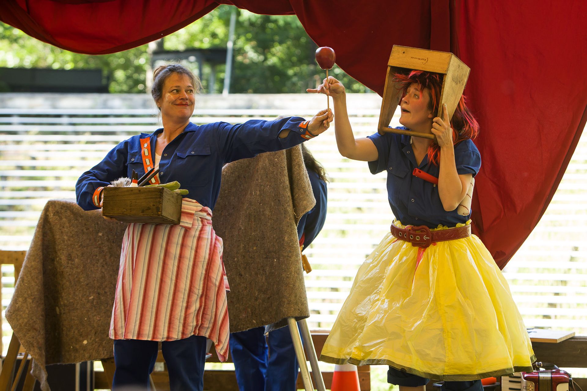 Zwei Performerinnen tragen Kleidung, die dem Disneyfilm Schneewittchen nachempfunden ist, aber zusammengestellt aus Blaumännern, einem Rock aus gelben Mülltüten und ausgestattet mit Werkzeugkästen. Beide halten den vergifteten Apfel.